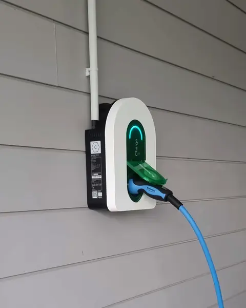 Borne de recharge Schneider Charge posée sur le bardage gris d’une maison, voyant allumé, câble bleu branché