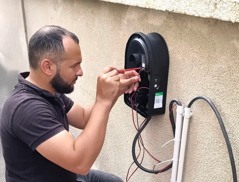 Le technicien d’Ave Green raccorde une borne de recharge murale noire fixée sur un muret, gaines grises à côté
