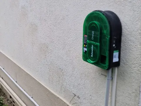 Borne de recharge fixée sur une façade, ses gaines grises posées le long du mur jusqu’au soubassement
