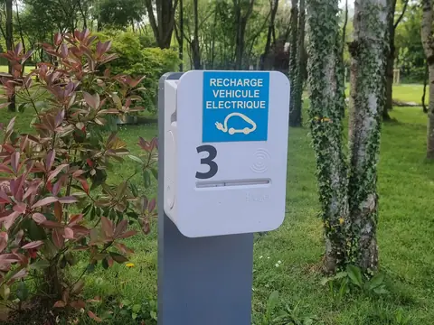 Borne de recharge sur pied Hager numérotée 3 sur le site d’une entreprise, entre la pelouse, les arbres et les massifs