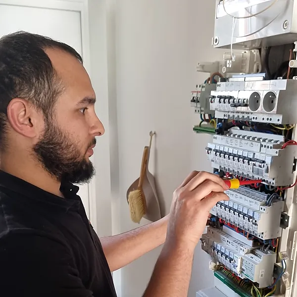 Le technicien d’Ave Green, de profil, serre un disjoncteur au tournevis isolé dans un tableau électrique ouvert