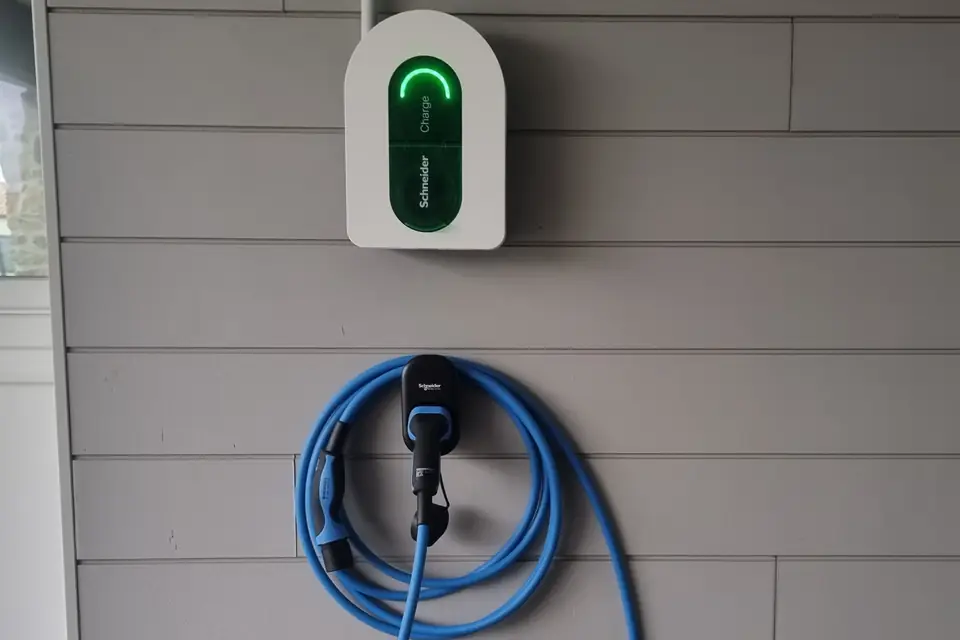 Borne Schneider Charge blanche au voyant vert sur un bardage gris clair ; son câble de recharge bleu est enroulé sur un support.