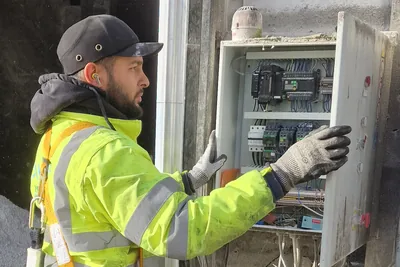 Technicien d’Ave Green en veste haute visibilité, harnais et gants, ouvrant une armoire électrique sur un site professionnel