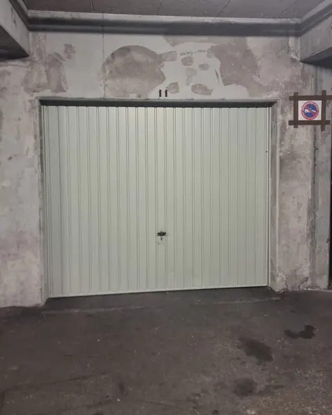 Porte de box vert pâle dans un parking souterrain, chemin de câbles au plafond