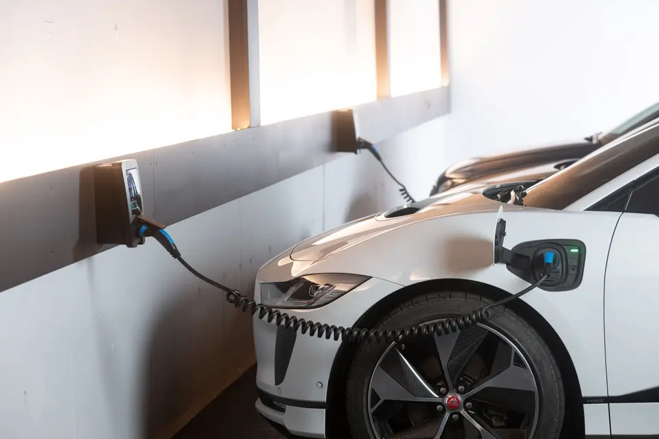 Voiture électrique blanche en charge sur sa place de parking, branchée à une borne murale fixée au mur du garage