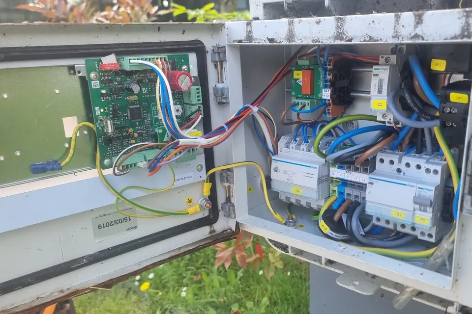 Borne de recharge sur pied ouverte : carte électronique dans la porte, modules Hager et borniers repérés d’étiquettes jaunes