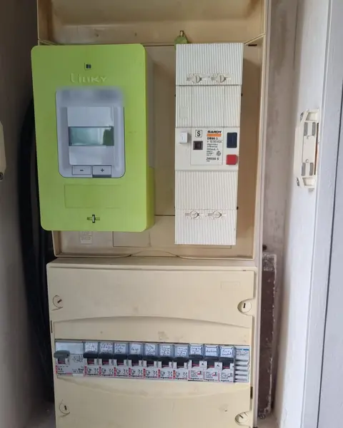 Niche technique avec compteur Linky vert, disjoncteur de branchement et tableau électrique ancien jauni aux disjoncteurs étiquetés à la main