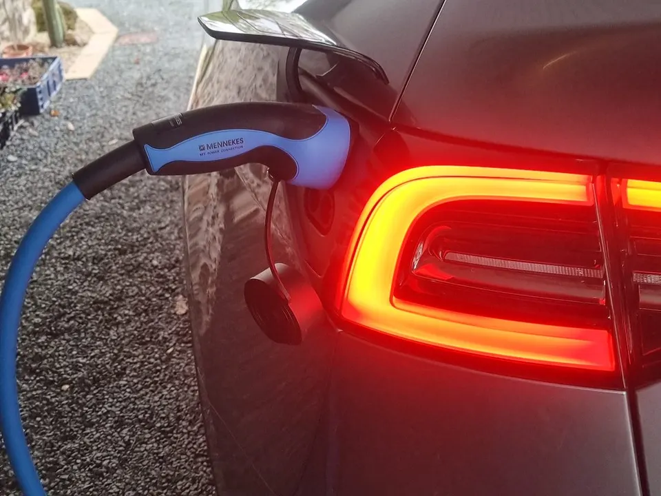 Voiture électrique grise en charge : pistolet de recharge bleu et noir branché dans la trappe, à côté du feu arrière allumé