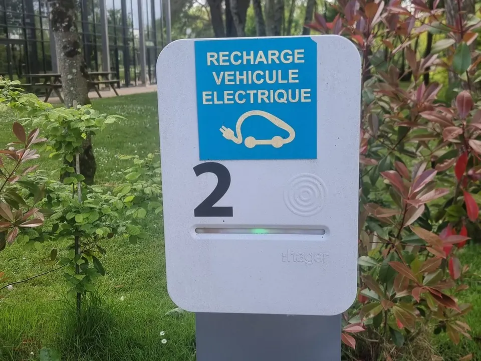 Borne de recharge sur pied numéro 2, autocollant « Recharge véhicule électrique », zone de lecture de badge et voyant vert, dans les espaces verts d’un site de bureaux