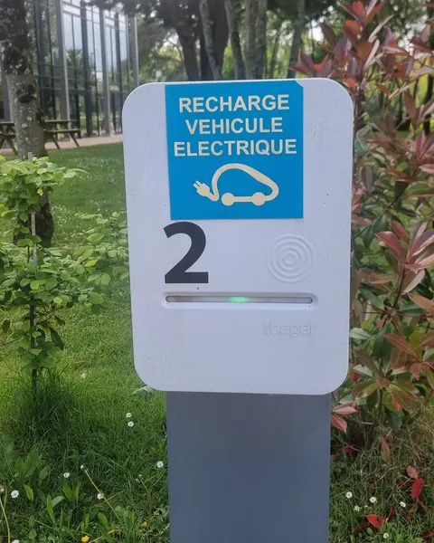Borne de recharge sur pied numéro 2, autocollant « Recharge véhicule électrique », zone de lecture de badge et voyant vert, dans les espaces verts d’un site de bureaux