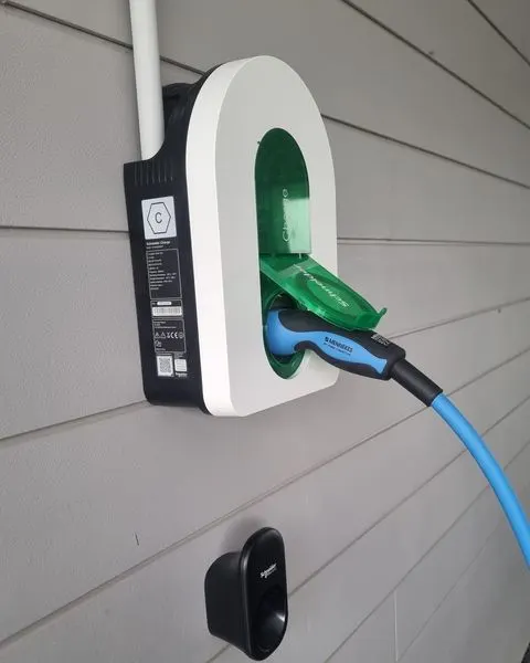 Borne Schneider Charge blanche fixée sur un bardage gris clair, clapet vert ouvert, câble de recharge bleu branché
