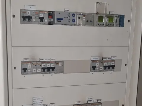 Armoire électrique ouverte d’un local technique, vue de près : modules de mesure et rangées de disjoncteurs étiquetés
