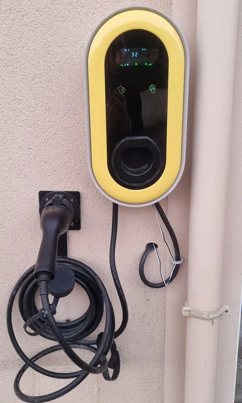 Borne murale à cadre jaune fixée sur une façade, son câble de recharge noir enroulé sur un support fixé au mur, hors du passage