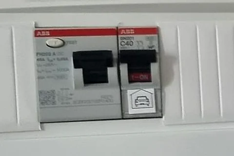 Gros plan d’un petit coffret électrique : un interrupteur différentiel et un disjoncteur marqué d’un pictogramme de voiture, rien que pour la borne
