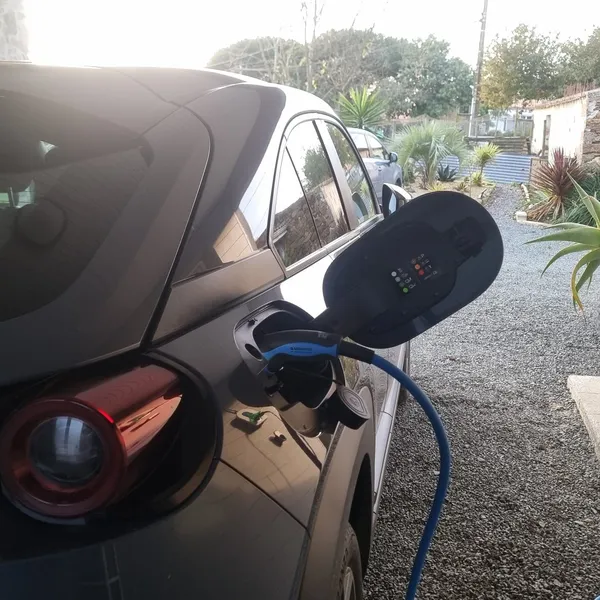 Une voiture en charge dans une allée gravillonnée, le câble bleu branché sur sa trappe arrière