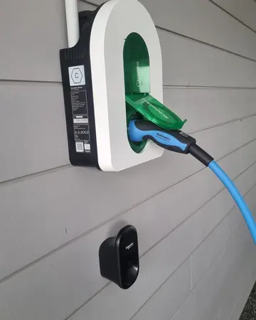 Borne de recharge Schneider Charge posée sur le bardage d’une maison, câble bleu branché