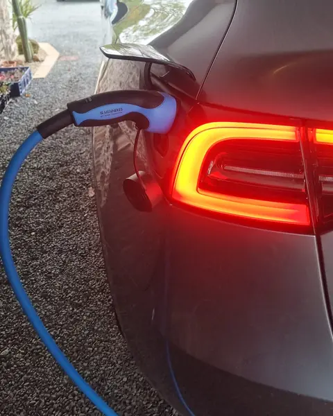 Pistolet de recharge à câble bleu branché dans la trappe d’une voiture électrique grise, à côté du feu arrière allumé