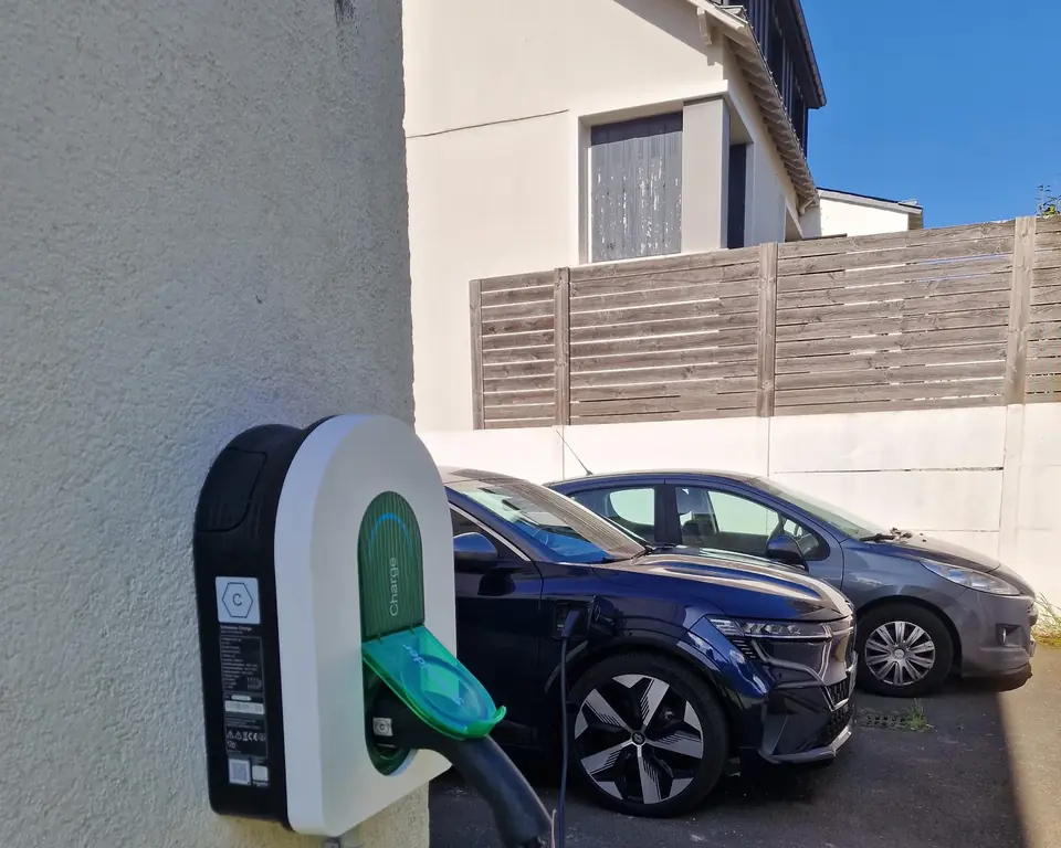 Voiture électrique bleu nuit en charge sur une borne murale, dans l’allée d’une maison
